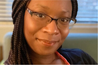 Stephanie Folarin is an African American woman smiling with glasses and braided hair