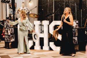 Two women in nice dresses standing on stage holding microphones