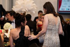 The backs of women, one standing and the other sitting, smiling at each other