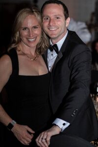 A man in a black tux and woman in a black dress smiling at the camera